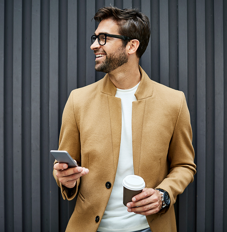 A young man holding a smartphone to buy shares online and a coffee cup