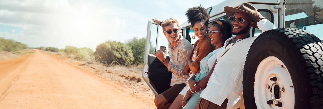 Young adults leaning against their vehicle in the bush on safari