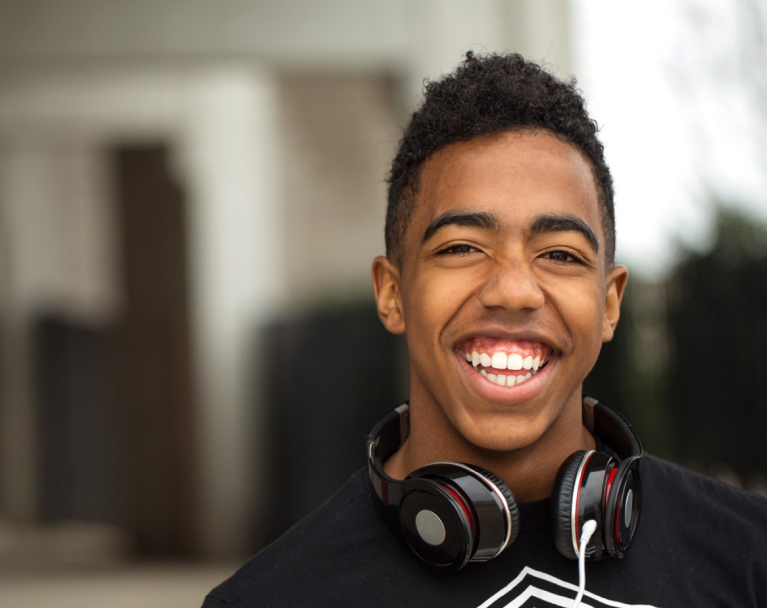 A teenager with headphones at school smiles at the camera