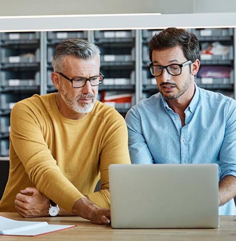 Two men talking over a laptop at a shop counter