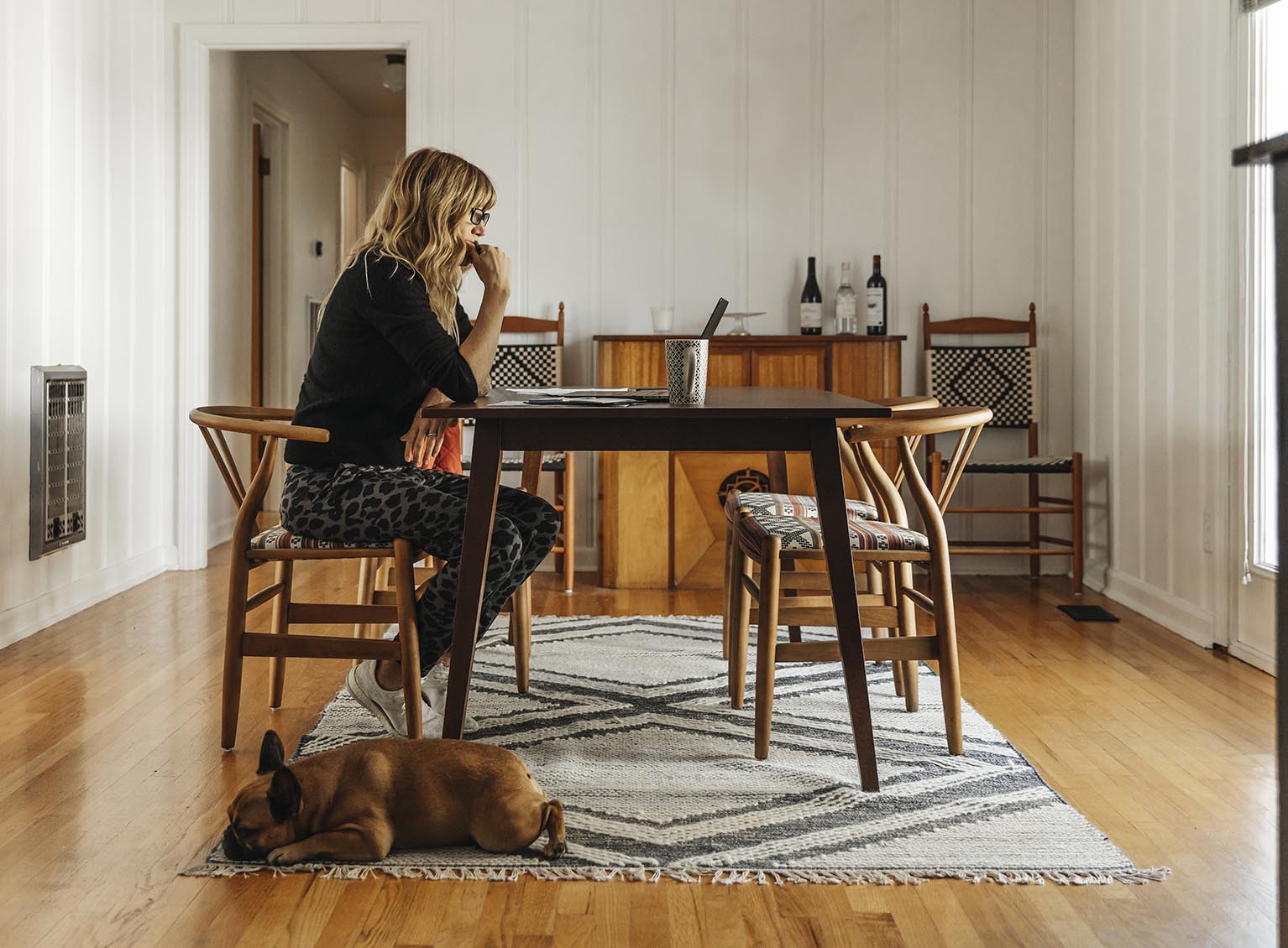 Woman sitting at a table in her house with dog at her feet