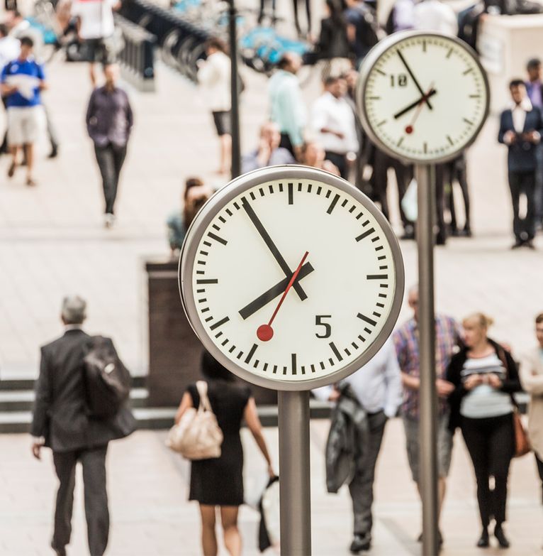 Crowds of office workers walk under the clocks of Canary Wharf