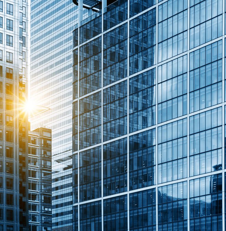Looking into a corporate skyscraper while the sun breaks past the building next to it