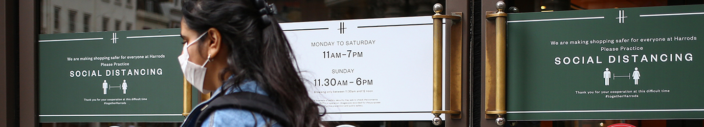 Woman walks past a reopening shop outlining social distancing rules