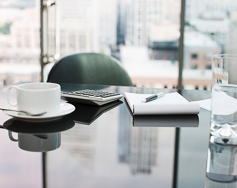 empty chair at an executive desk with writing pad, coffee cup and water glass