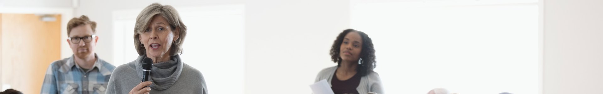 A lady stands amongst a crowd to speak at a community charity meeting