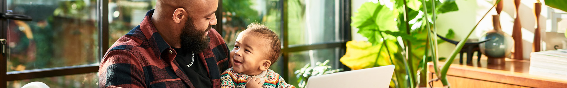 Father sitting with child on his lap while working on laptop at kitchen table