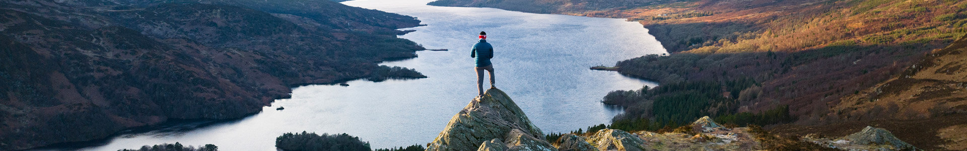 Male standing on top of a rock looking down at a lake and surrounding mountains