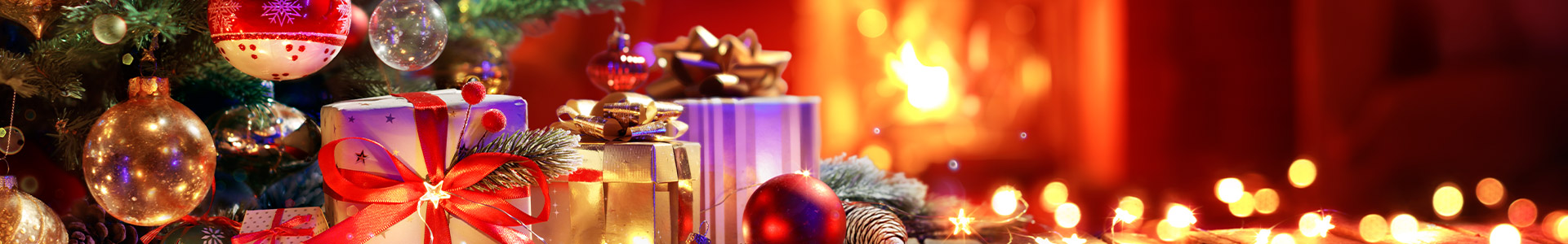 Decorated Christmas tree with presents underneath sitting infront of a fire