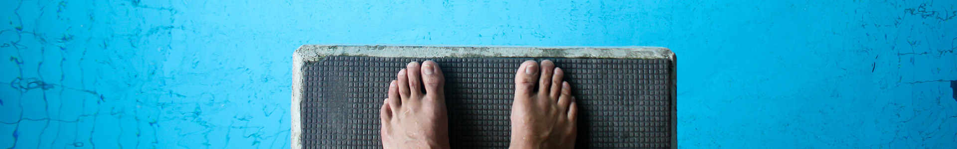Feet on edge of diving board ready to jump into the pool