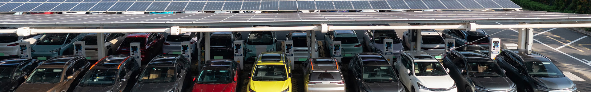 Electric cars all parked and charging in a row under a shelter with solar panels on the roof