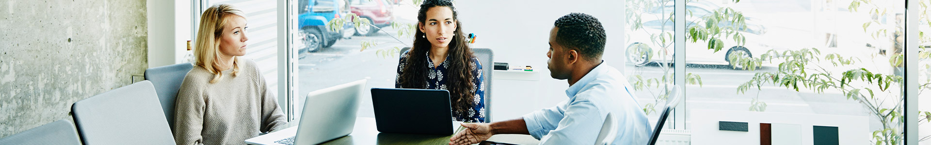 Three people discussing business around a meeting table