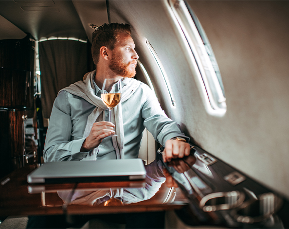 Successful business man sitting on private plane with glass of wine