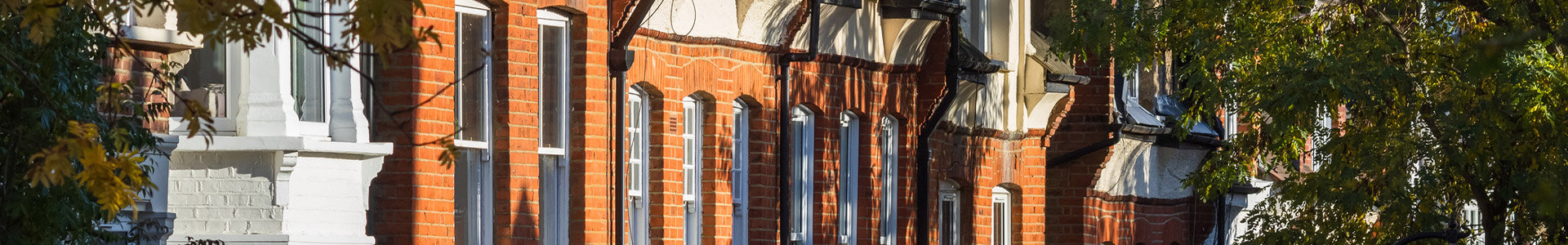 Facade of traditional English terraced houses partially in the shade of trees in London