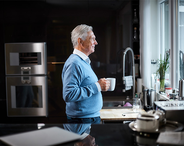 Male standing in his kitchen looking out over his garden with a cup of tea