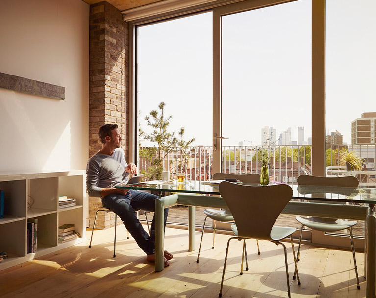 Male sitting at table looking out of window in his flat