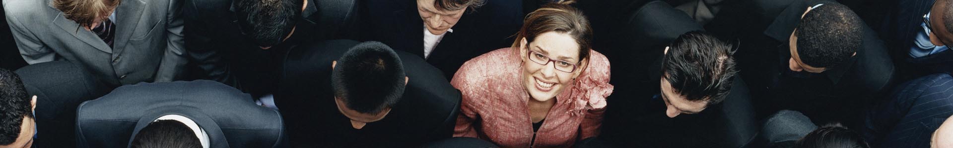 Businesswoman Looking up at Camera and Standing Outdoors Surrounded by a Large Group of Business People
