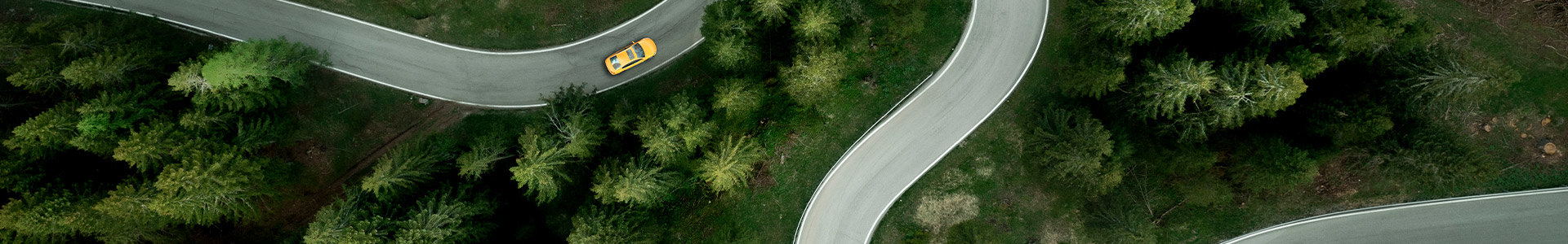 Aerial view of a car traveling on a winding mountain road in a forest