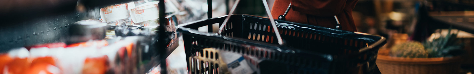Female shopper holding basket in supermarket checking the contents on a jar