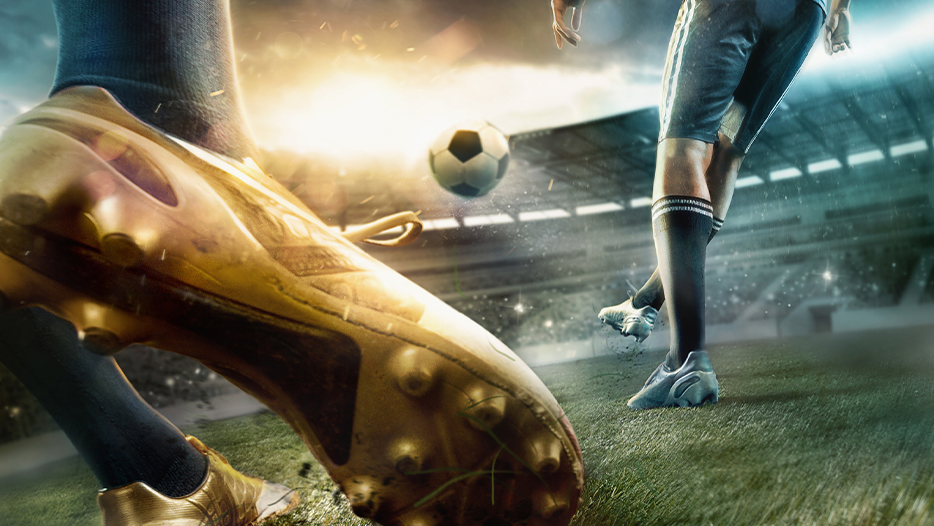 Close up of football boots with a football player in background kicking football in a stadium