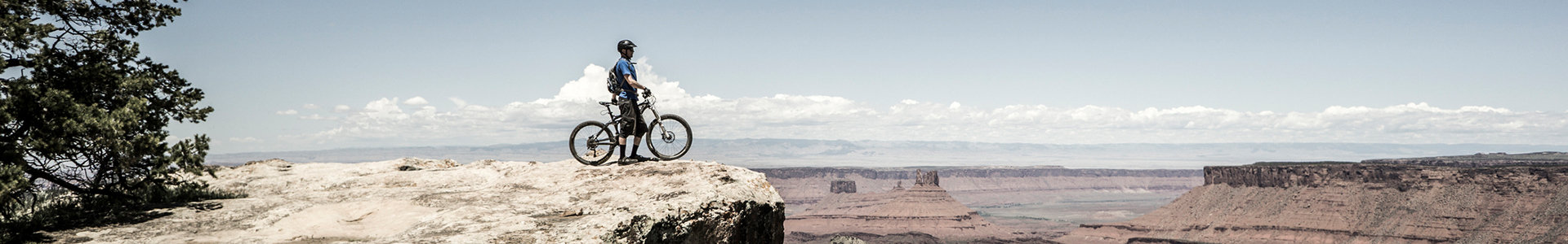 Male mountain biker standing near edge of cliff face with bike looking down at scenery
