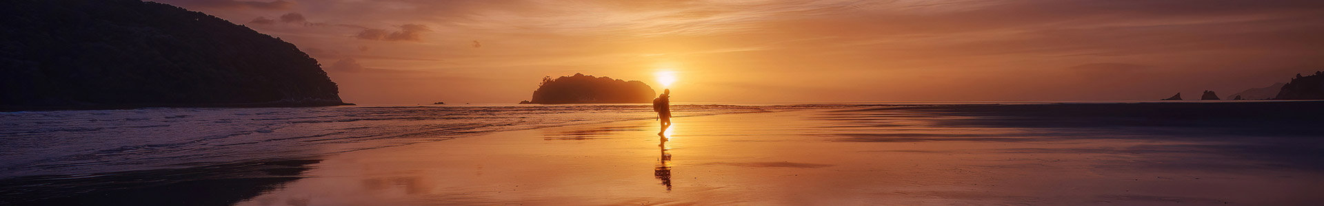 Single person walking across beach as tide goes out at sunset