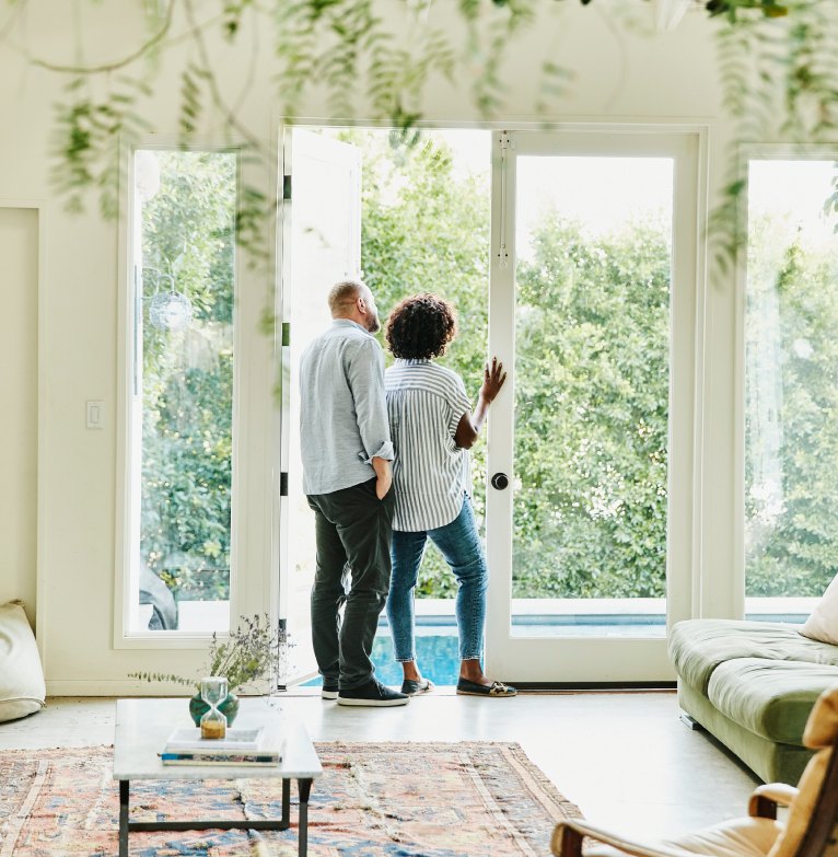 A couple standing together look out from their house into their garden