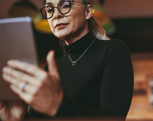 A woman in glasses looks at her tablet