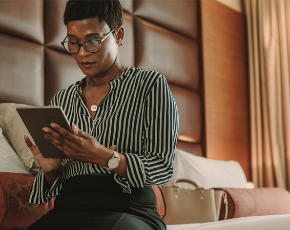 A lady sits on a hotel bed while reading something on her tablet