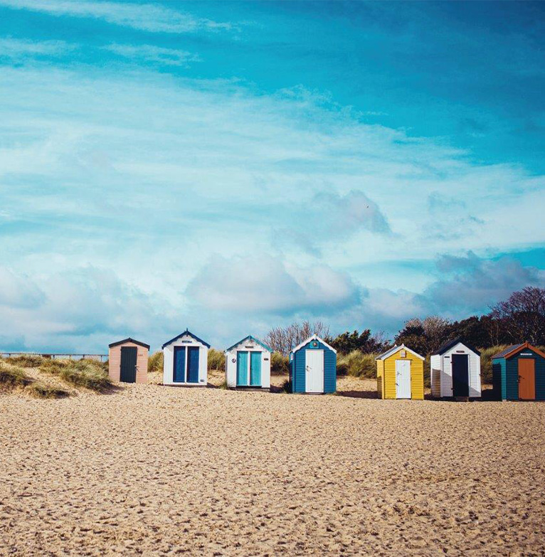 A line of colourful beach huts sit on the sand at the beach