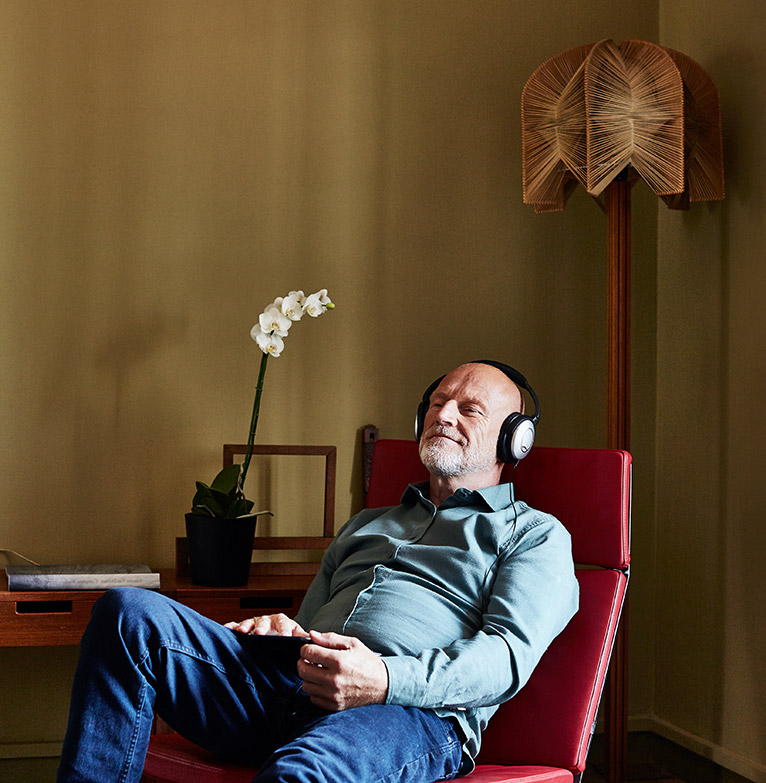 An older man relaxes in a chair listening to music through headphones