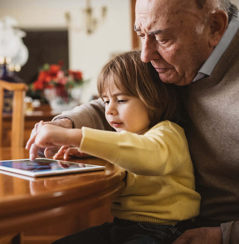An elderly man looking at his tablet with his grandchild