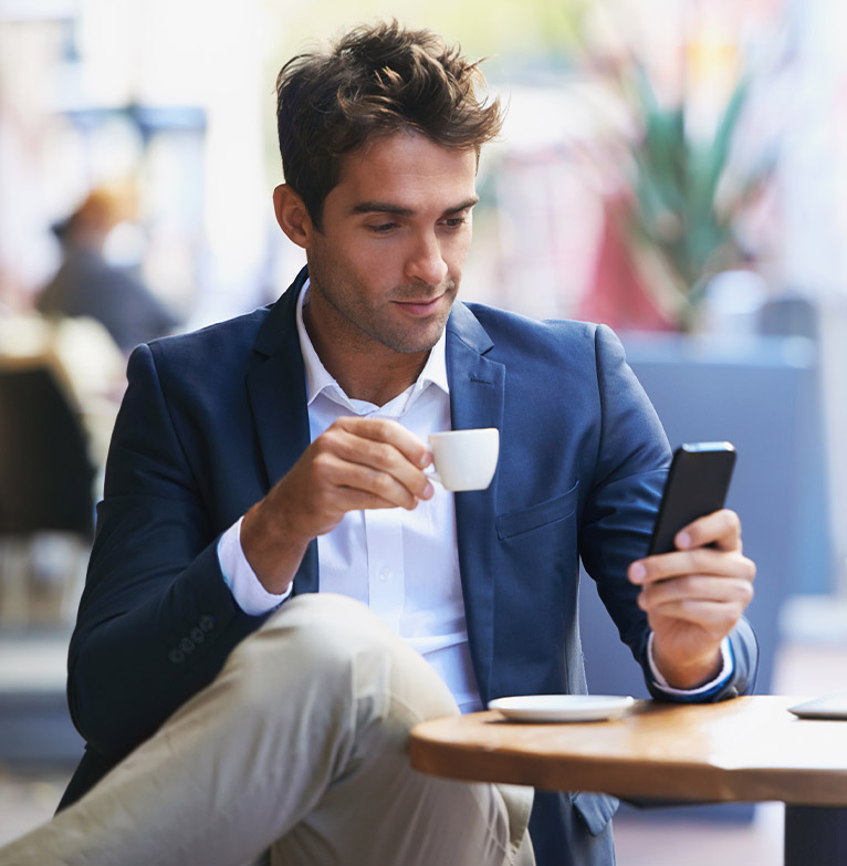 High net worth male sipping an espresso and checking his phone at cafe table