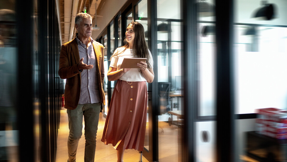 A woman and man conversing while walking through an office