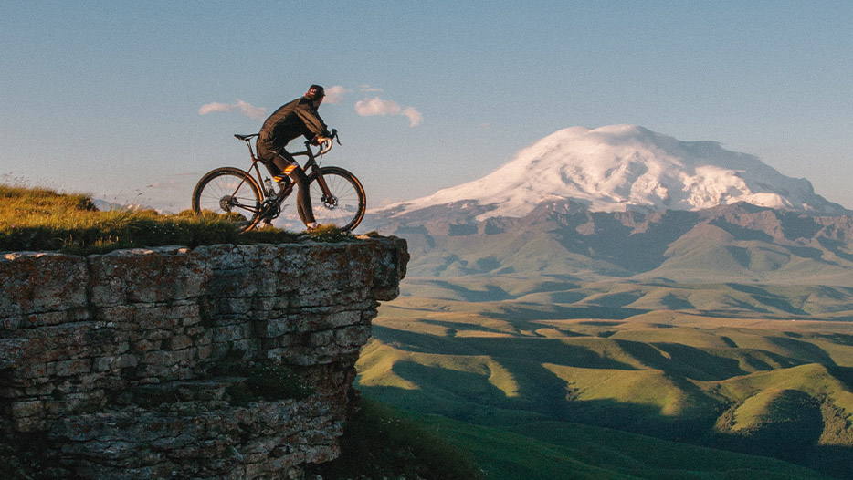 Person sat on their bike at the edge of a cliff looking out at mountain range in distance
