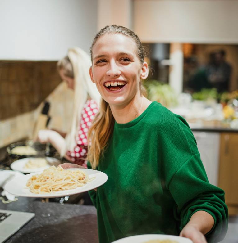 A lady laughs while handing dinner to someone in a charity kitchen