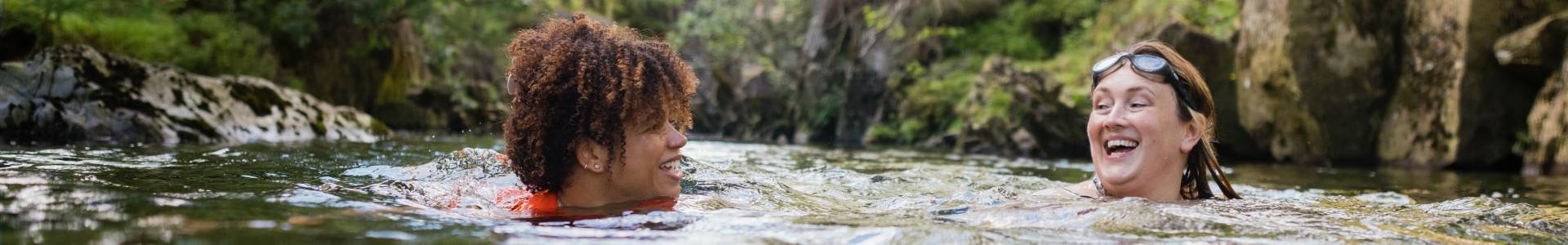 People wild swimming in a river lined with green trees
