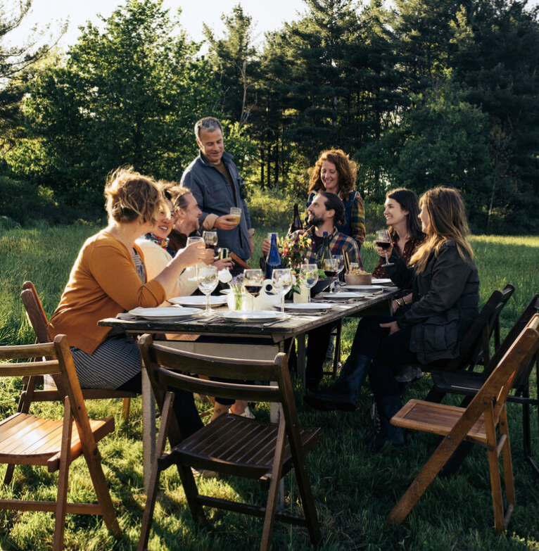Friends and family chatting together at a dining table in a field having a lunch outdoors