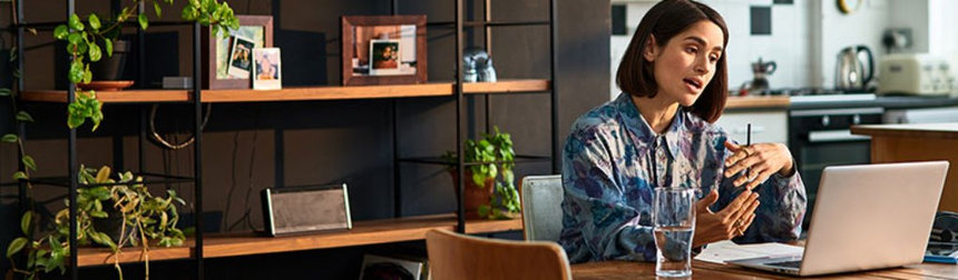 A lady speaks into a laptop during a webinar at her kitchen table