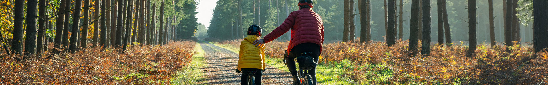 Father holding his son to help him balance as they both cycle along a path in the forest