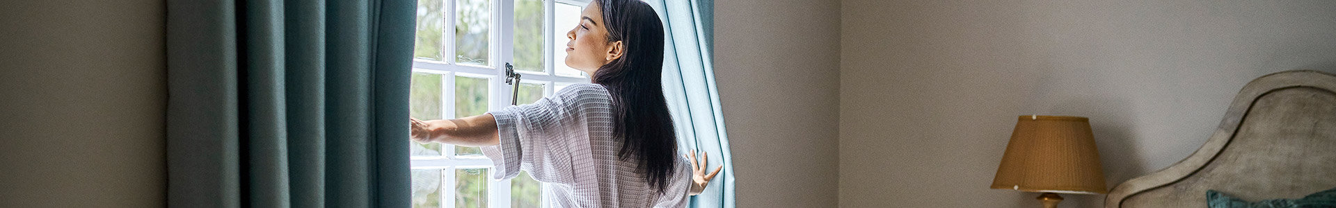 Female contemplating her wealth during divorce while opening curtains in the bedroom