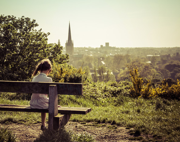 a young girl sitting on a bench looking over a city