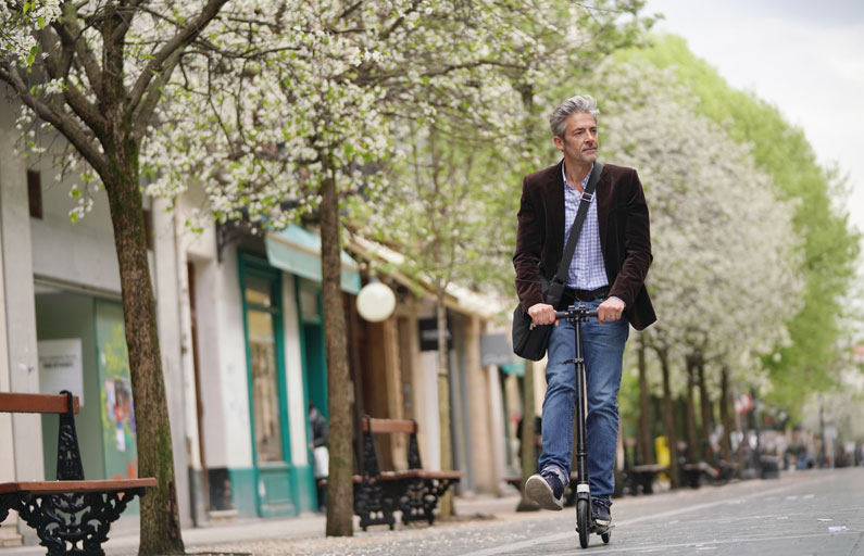 Middle-aged man on a scooter travels down a tree-lined street