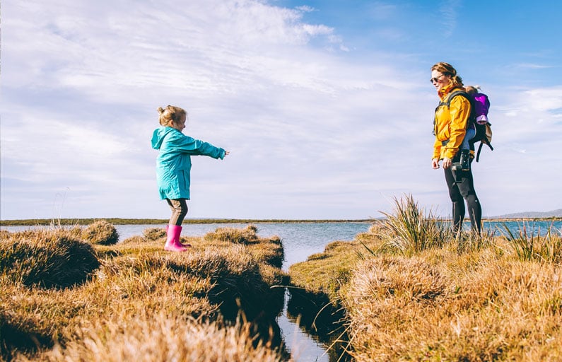 Mother and daughters in bright coats walking along a lake