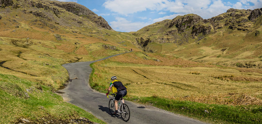 Person cycling up a windy road going between two hills