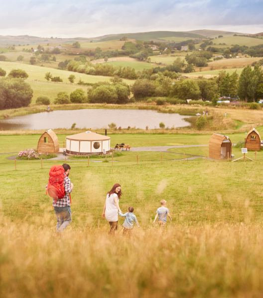 A young family walk down the hill to a glamping site in the British countryside