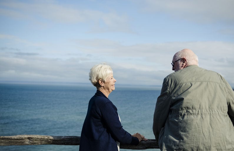 Elderly couple smiling at each other on a windy coastal lookout