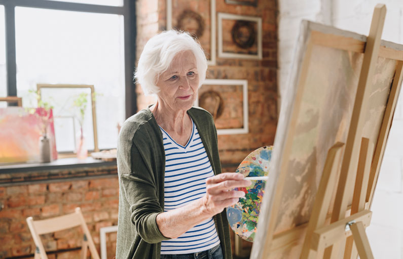 Elderly woman paints on a canvas in a light-filled room