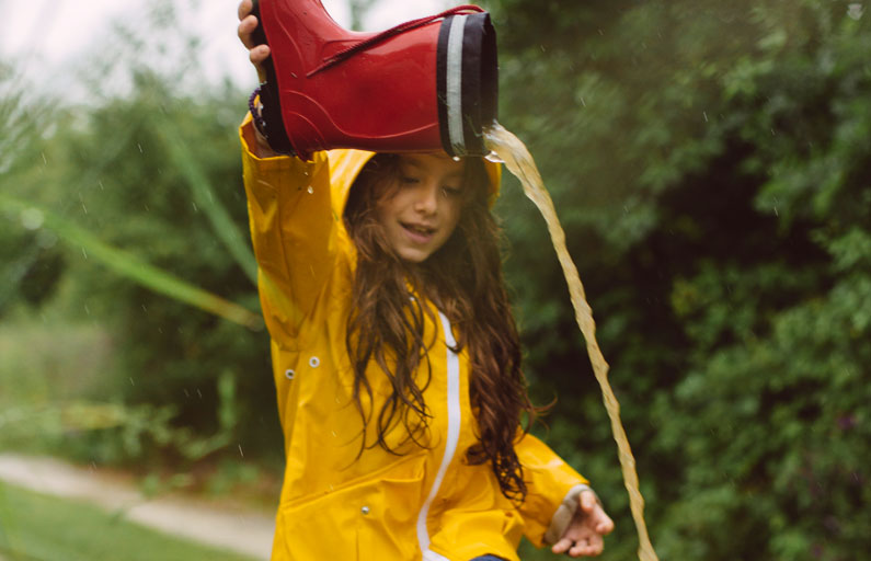 Girl in yellow raincoat empties welly full of puddle water