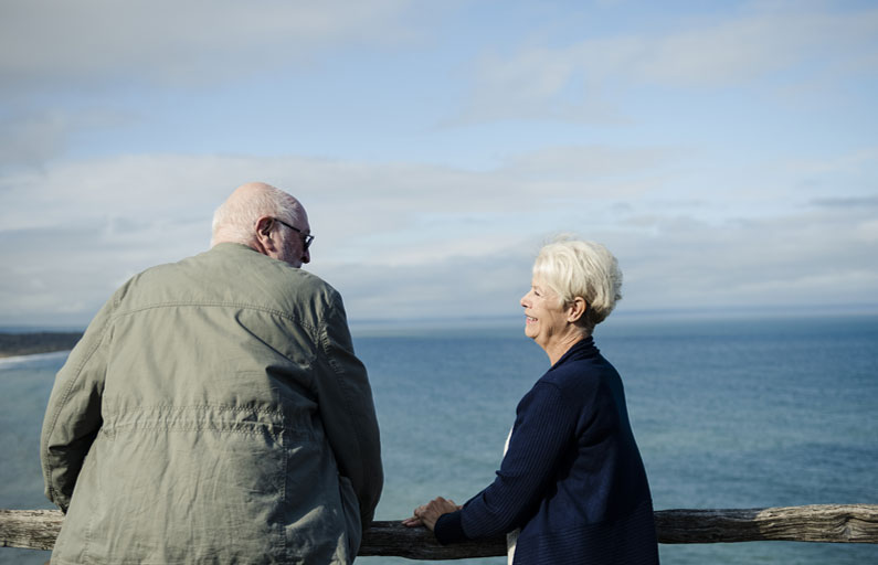 Elderly couple smiling at each other on a windy coastal lookout